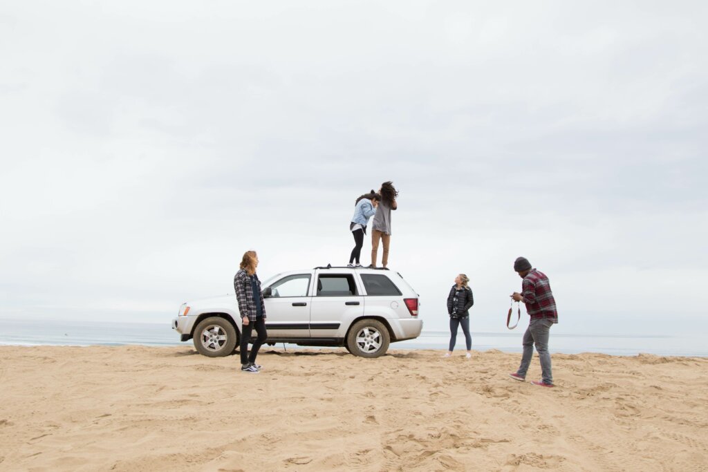 Grupo de amigos em uma praia, se divertindo ao redor de um carro, felizes pois encontraram o melhor preço de baterias
