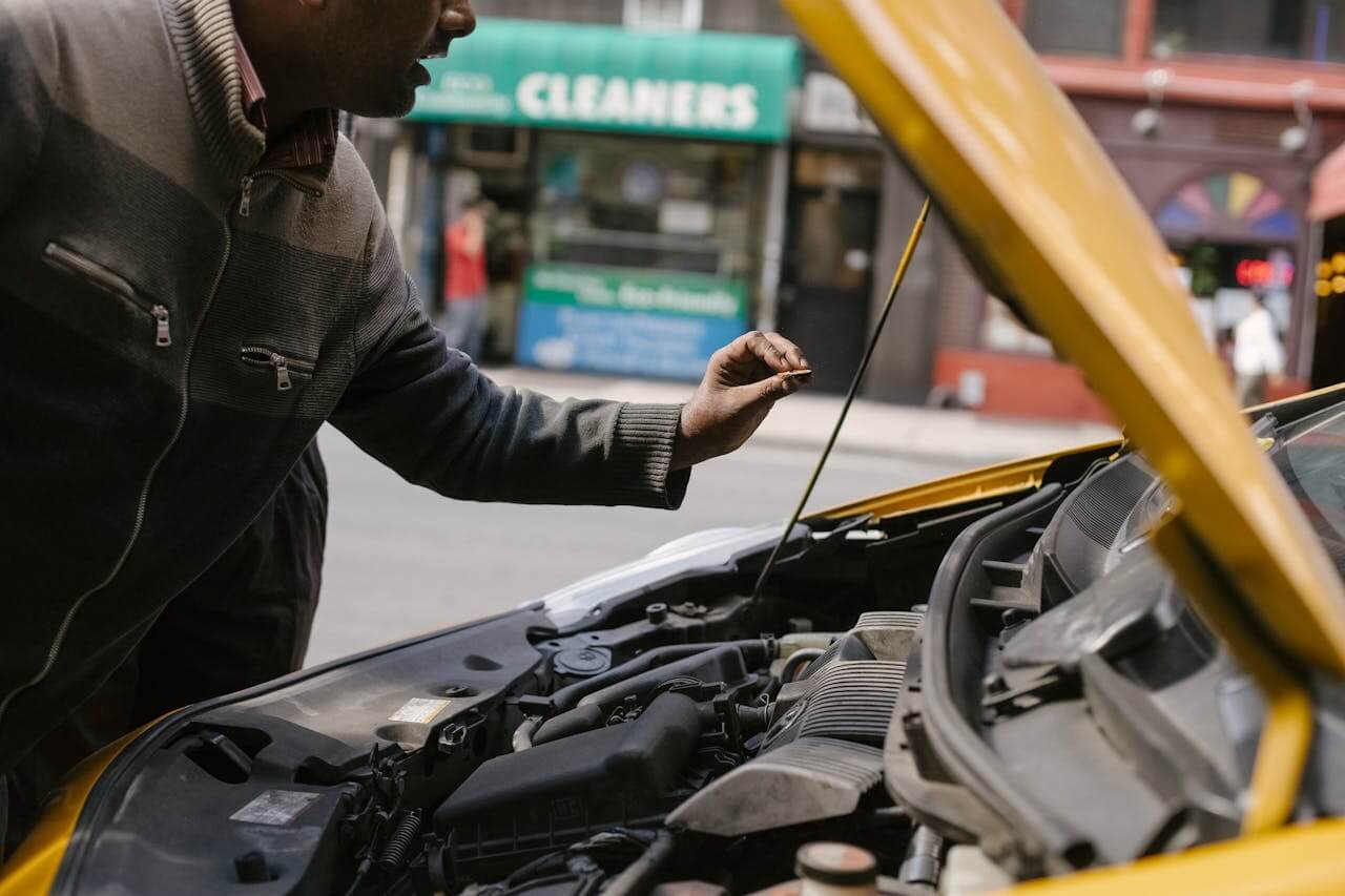 Homem verifica o motor de um carro com o capô levantado, inspecionando possíveis problemas enquanto o veículo está estacionado na rua.