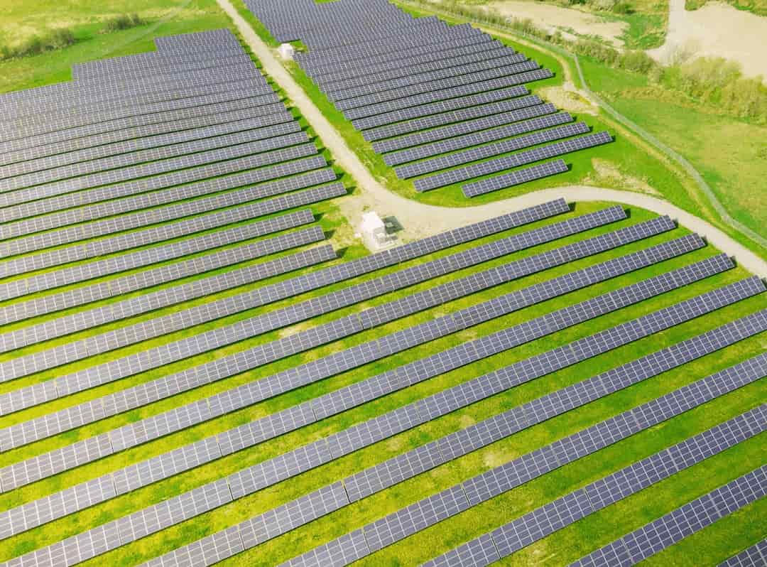 Vista aérea de um extenso sistema fotovoltaico em um campo, mostrando fileiras ordenadas de painéis solares capturando energia solar em um dia claro.