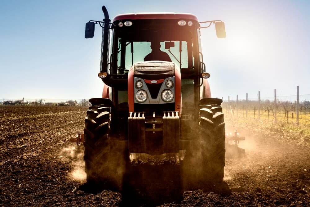 Trator arando a terra em campo com luz solar ao fundo.