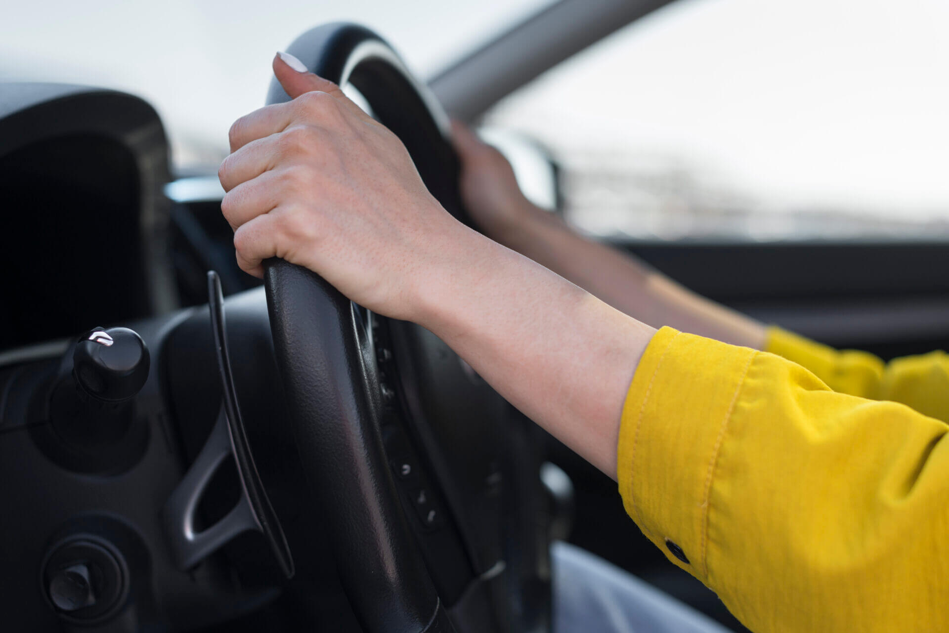  Mãos femininas postas no volante de um carro.