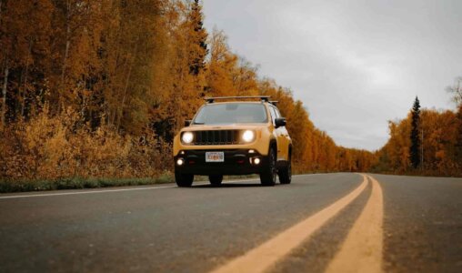 SUV amarelo equipado com motor a diesel viajando por uma estrada cercada por árvores de folhas amarelas no outono, destacando a eficiência e durabilidade dos motores a diesel em viagens longas.