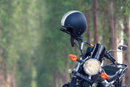 Uma moto de estrada estacionada em uma via arborizada, com um capacete preto e branco pendurado no guidão.