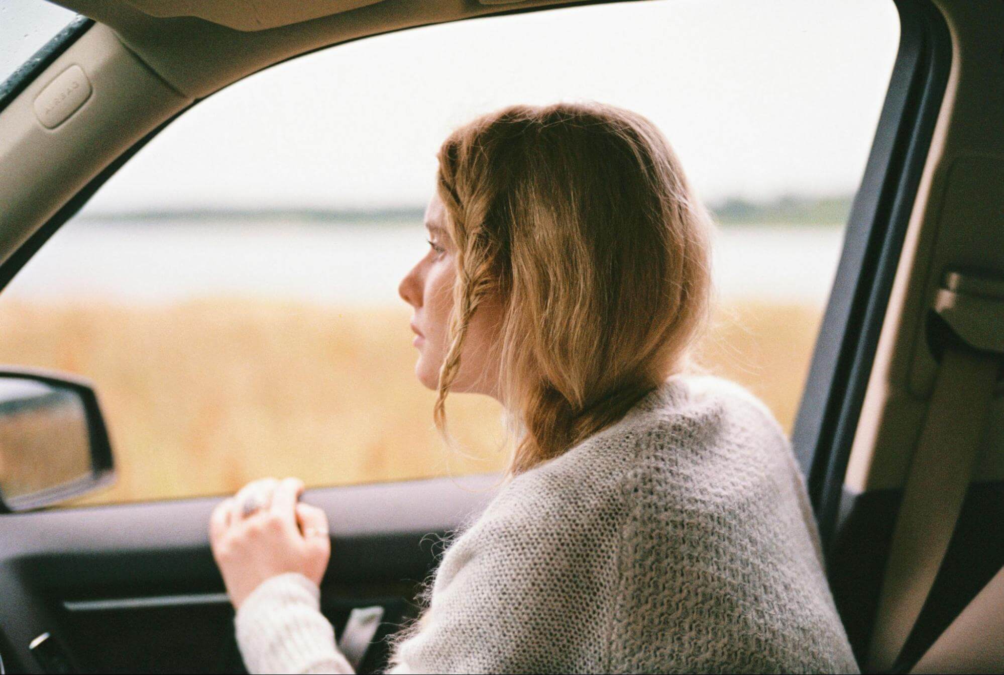 uma mulher de cabelos curtos está debruçada sobre uma janela de um veículo que está andando na pistaa