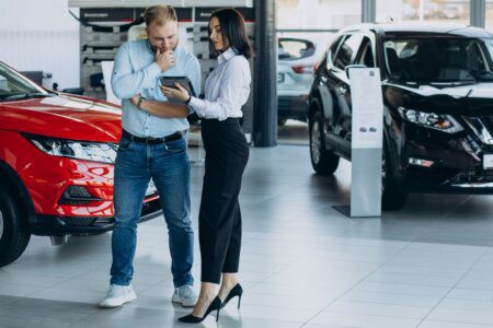 como comprar um carro: Homem em uma concessionária olhando um tablet mostrado pela vendedora