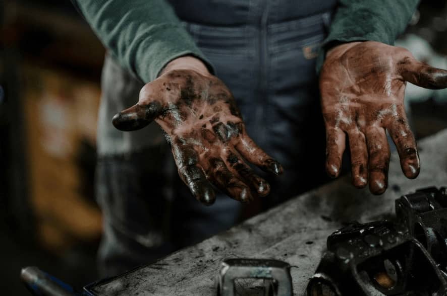 Mecânico mostrando as mãos sujas de óleo após trabalhar no corpo de borboleta e outros componentes do motor, destacando a natureza prática e exigente da manutenção automotiva.