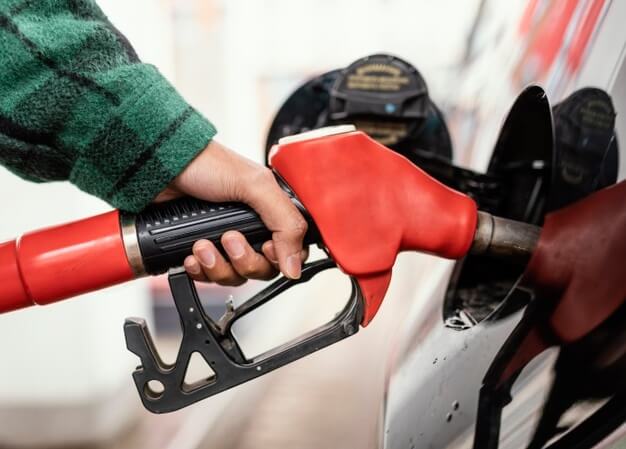 a mão de um frentista está segurando uma mangueira de combustível vermelha enquanto abastece um veículo