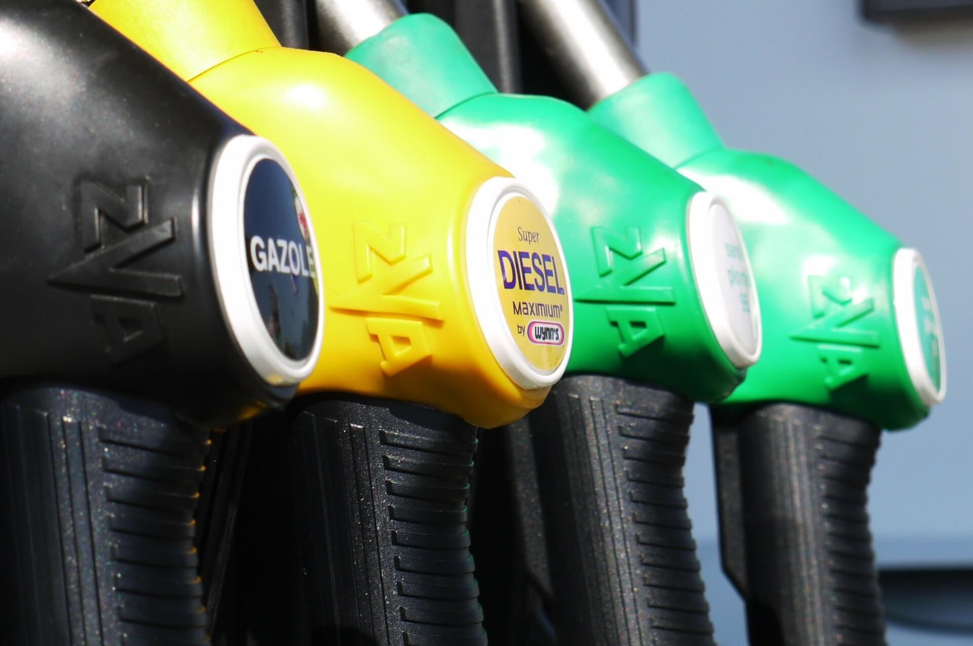 quatro mangueiras de combustível estão dispostas em sequência, no que parece ser um posto de abastecimento. Uma delas é preta, outra é amarela e as duas à direita são verdes