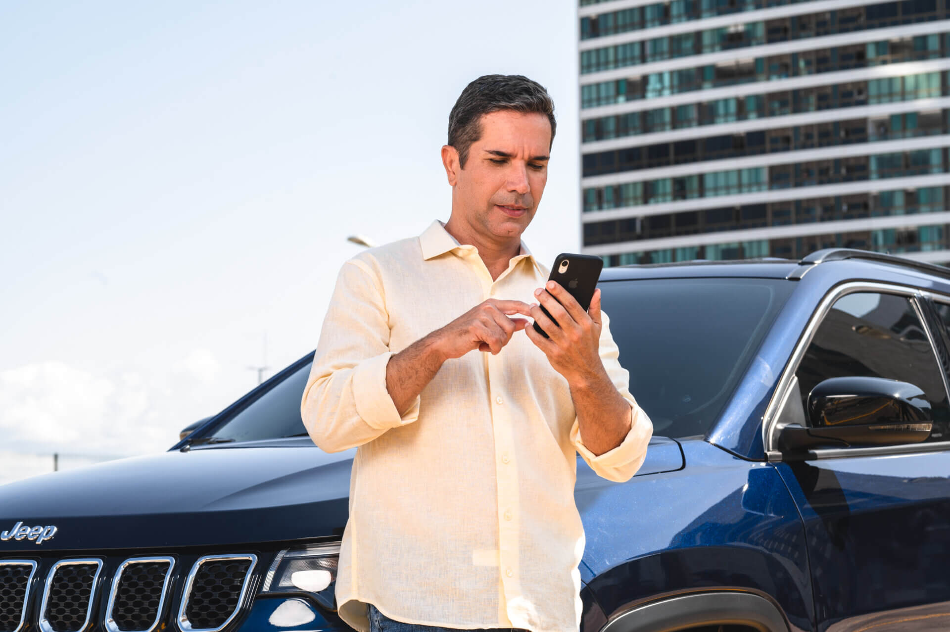 Homem branco apoiado em seu carro numa pista enquanto está no celular informando a Moura Fácil qual o modelo do veiculo.
