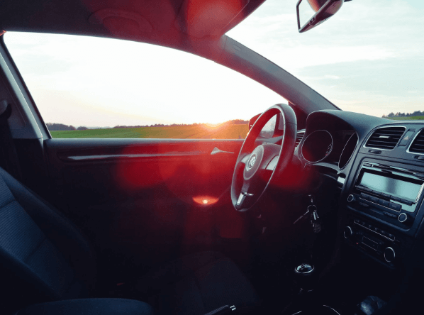 na imagem, o interior de um carro está parado em uma rodovia e, por meio do vidro que não contém insulfilm, a luz do sol está entrando 