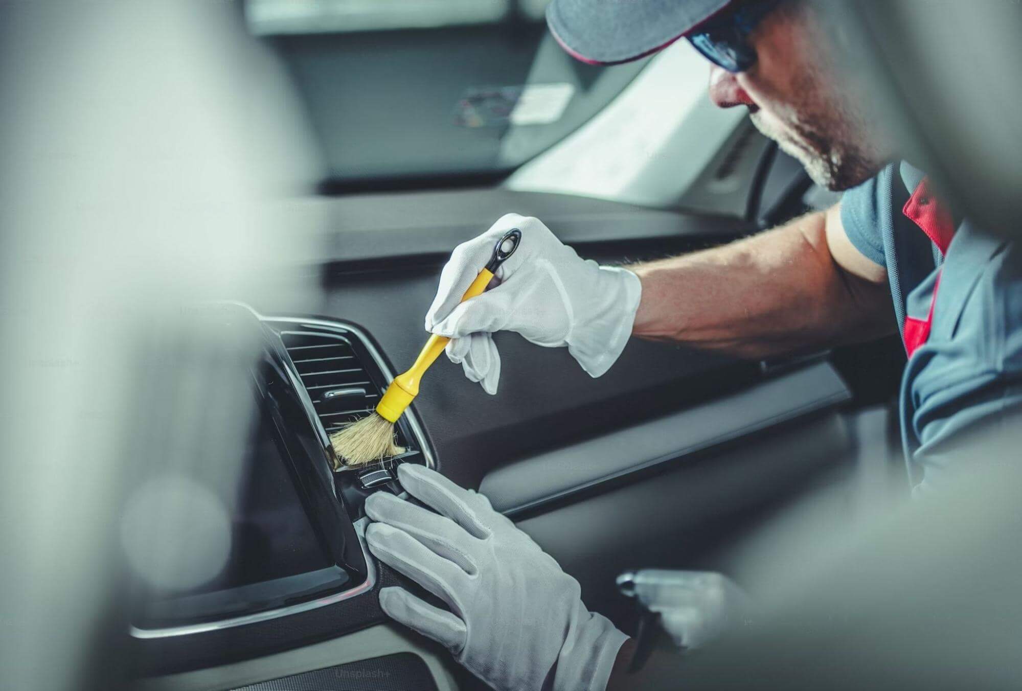 um profissional da área automotiva está utilizando equipamentos de limpeza para retirar partículas e sujeiras das grades de um ar condicionado automotivo