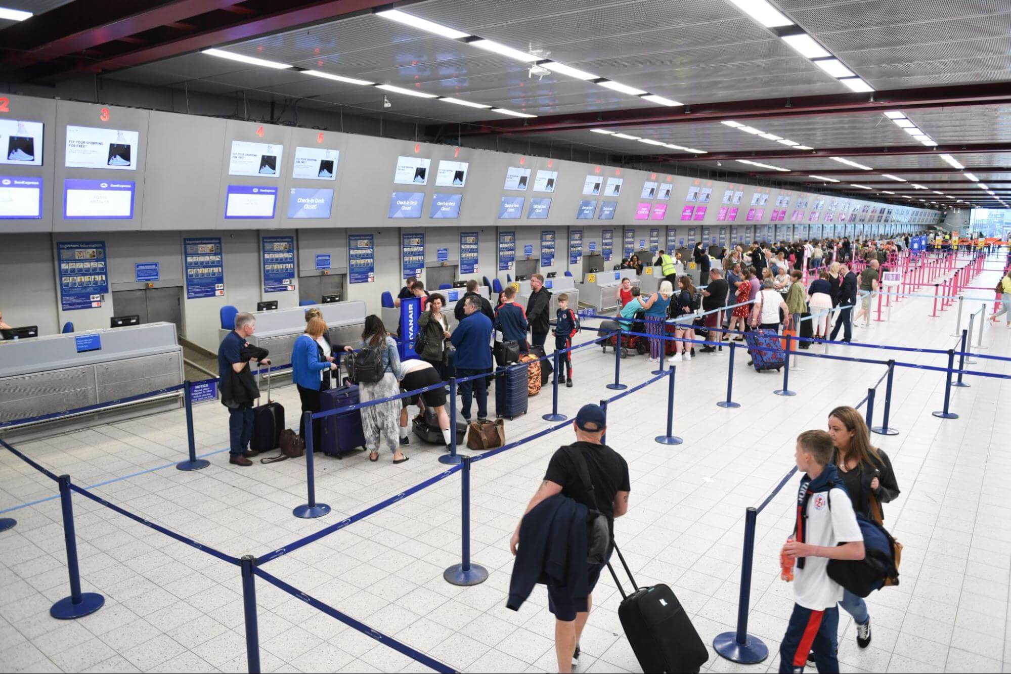 A área de embrarque de um aeroporto é mostrada de cima, onde pode-se ver diversas pessoas em fila para apresentar documentos