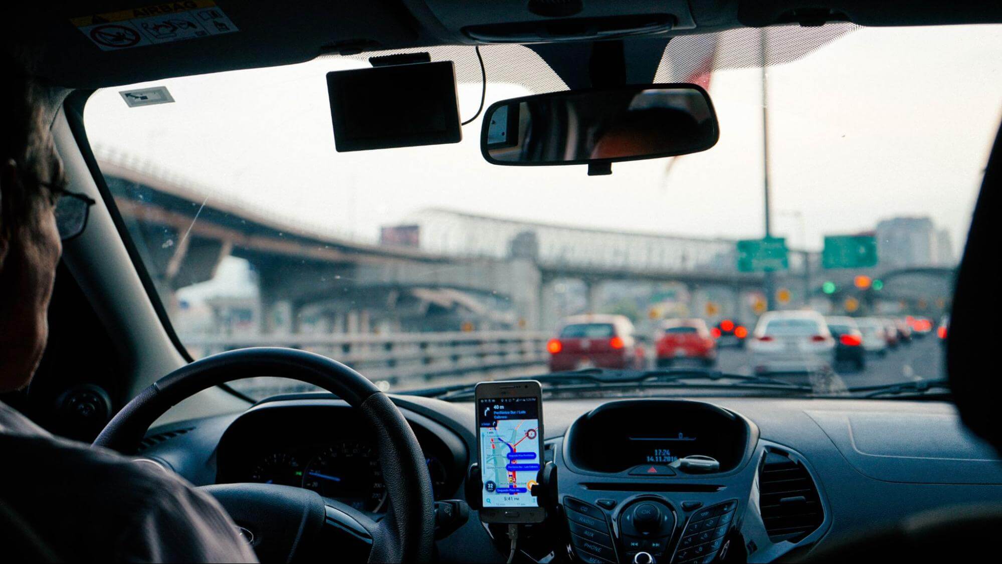 o interior de um carro e seu painel estão em foco, com o celular fixado no porta-celulares