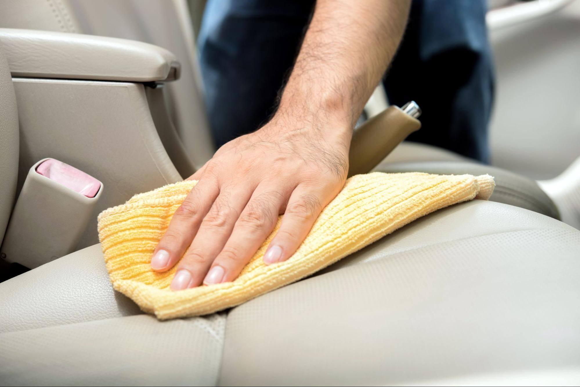 uma mão humana está passando um pano de limpeza sobre os bancos de couro de um carro