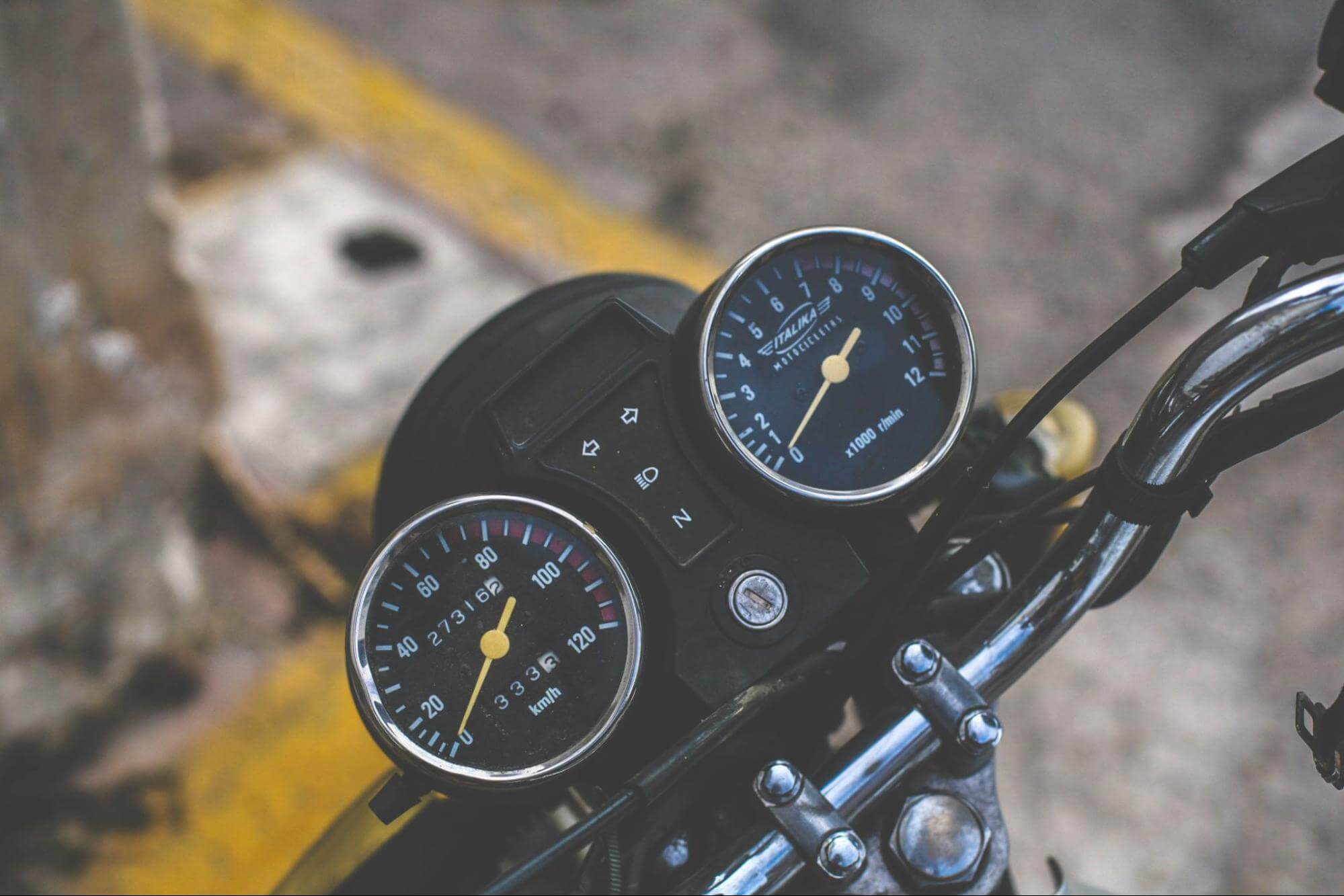 o hodômetro e o velocímetro de uma motoestão em foco. Essa moto está parada em um estacionamento ao ar livre 