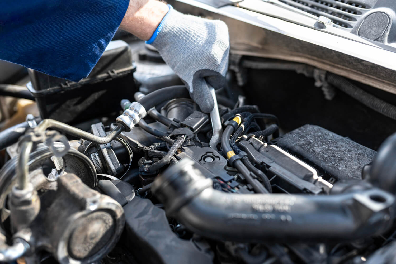 Foto de um mecânico com luvas ajustando componentes sob o capô de um carro, focando especialmente na limpeza e manutenção do bico injetor para assegurar o funcionamento seguro e eficiente do veículo.