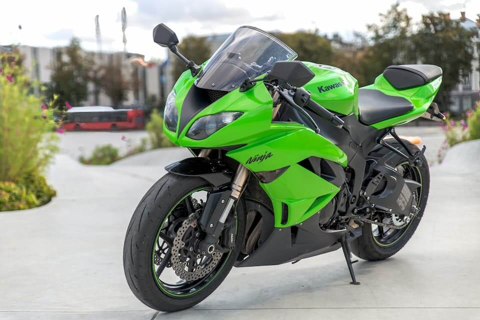 Moto Kawasaki Ninja verde estacionada em uma área urbana, destacando-se por seu design aerodinâmico e esportivo.