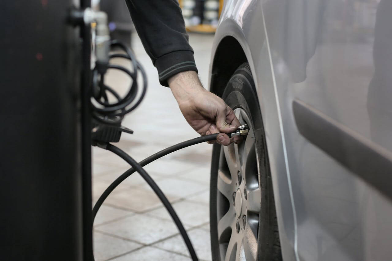 Uma pessoa segurando um cabo para calibrar os pneus de veículo. O cabo está conectado ao pneu de um veículo. O carro é prata. 