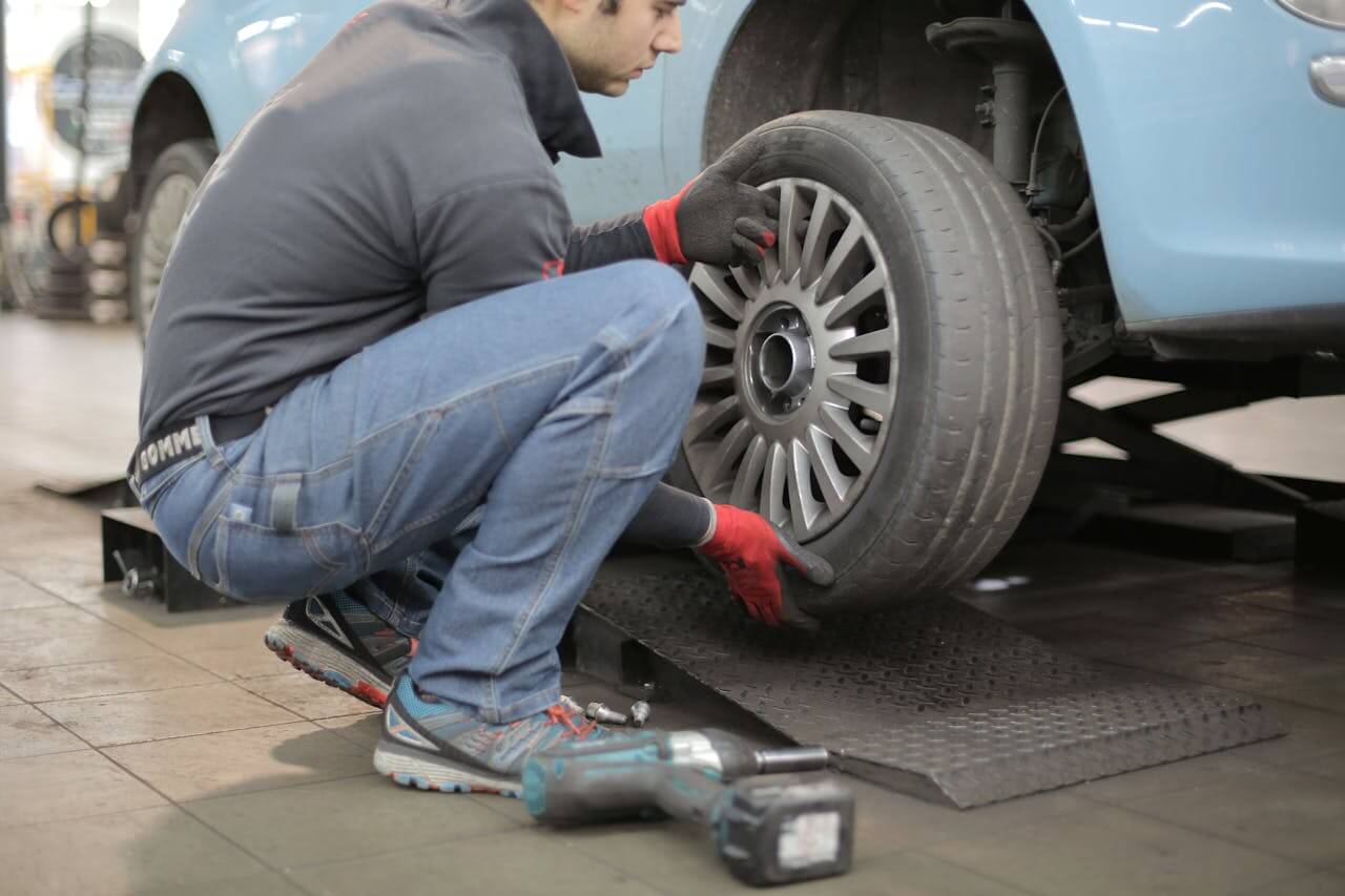 Um homem agachado em uma oficina, trocando o pneu de um carro azul. 