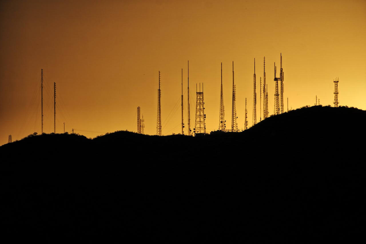 Silhueta de várias antenas de telecomunicação em uma colina ao pôr do sol, representando a aplicação das baterias nobreak VRLA em sistemas críticos.