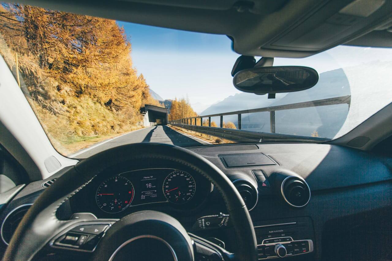 Vista interna de um carro em movimento em uma estrada montanhosa, mostrando o painel de controle e o volante, destacando a experiência de direção em diferentes condições de estrada.