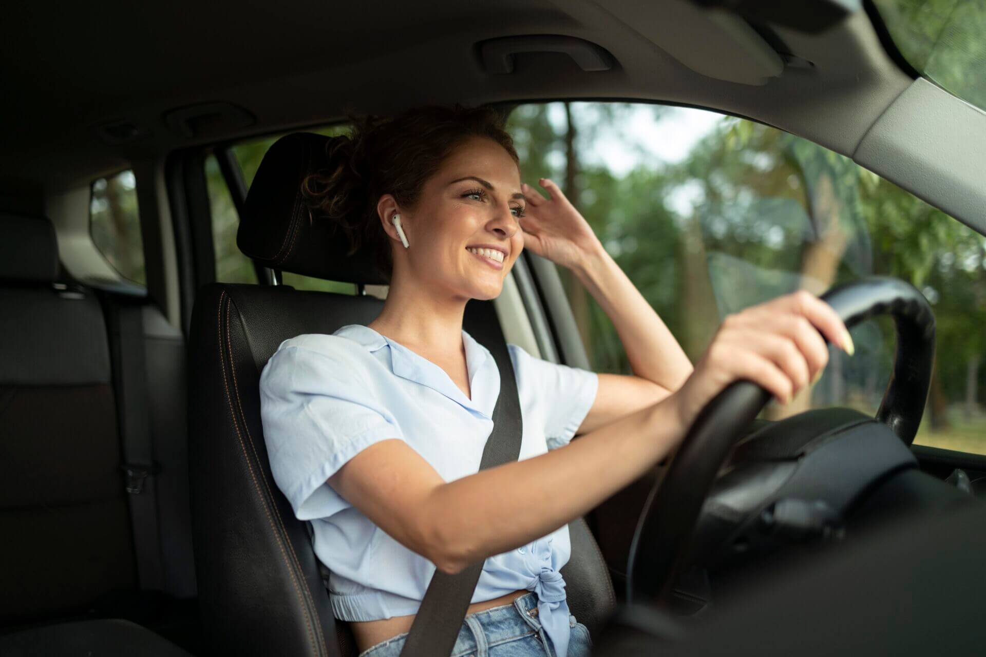 Mulher sorridente dirigindo um carro com fones de ouvido sem fio.