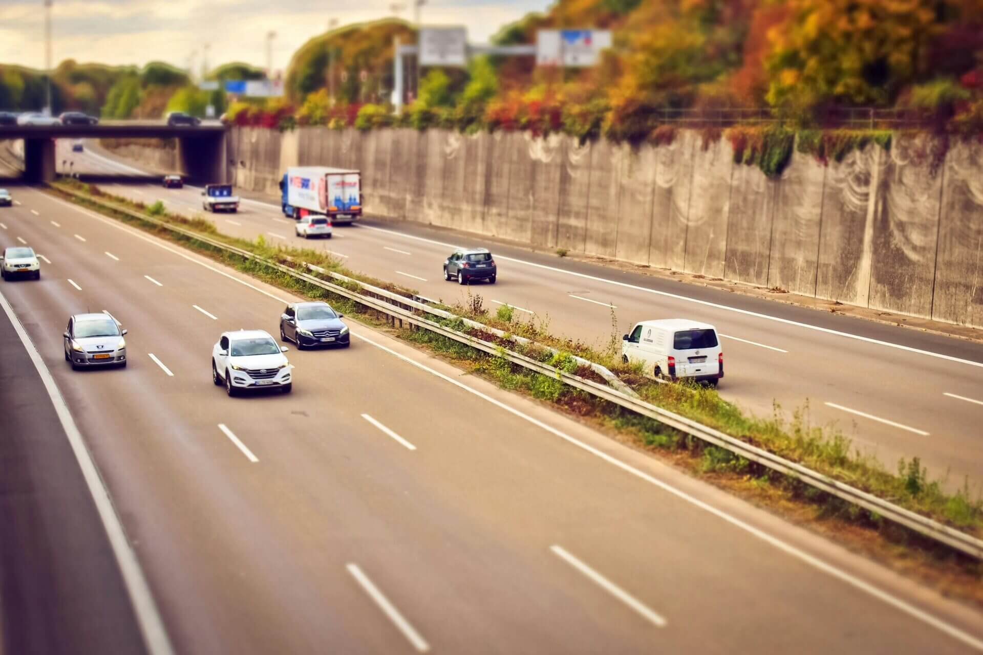 Visão panorâmica de uma rodovia com várias faixas, onde estão circulando diferentes veículos, incluindo carros de passeio, caminhões e uma van.