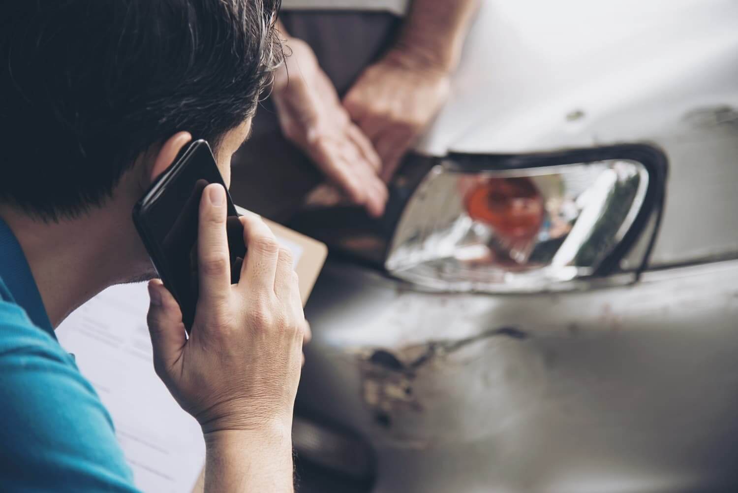 Homem falando ao telefone próximo a um carro danificado após acidente.