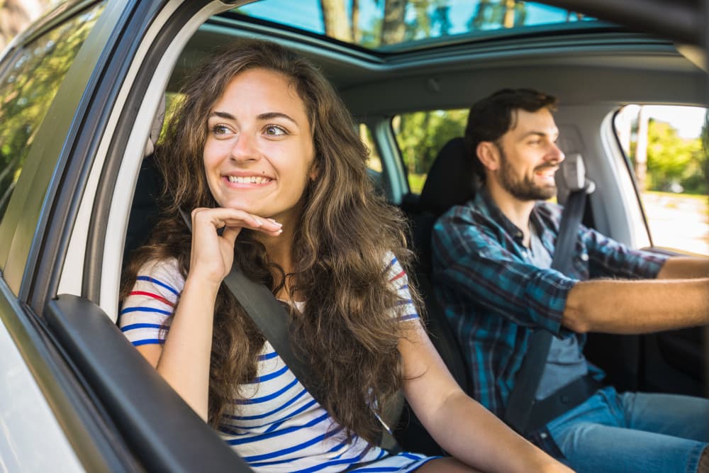 Mulher sorridente olhando pela janela de um carro, enquanto um homem dirige ao lado.