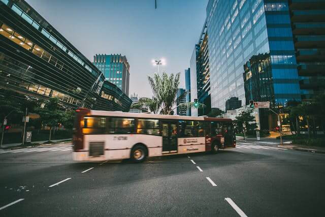 Ônibus em movimento em uma rua cercada por edifícios modernos ao entardecer.