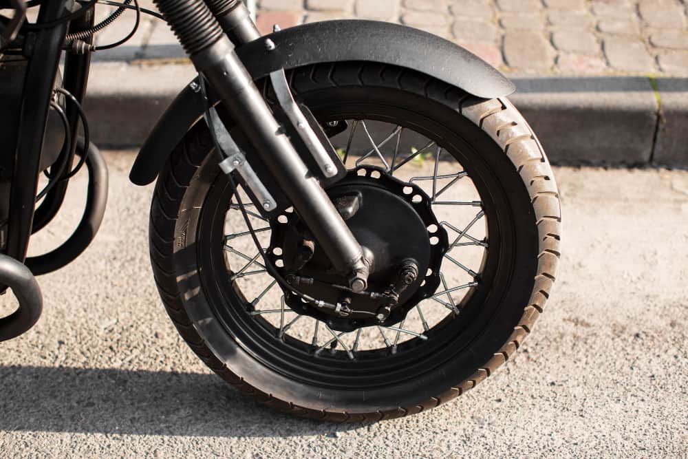 Roda dianteira de moto estacionada sobre o asfalto, com pneu bem calibrado e em boas condições.