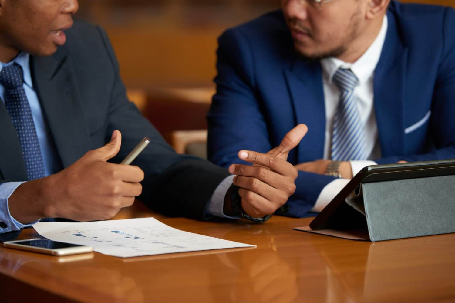 Dois homens de terno, sentados em uma mesa de escritório, conversando.