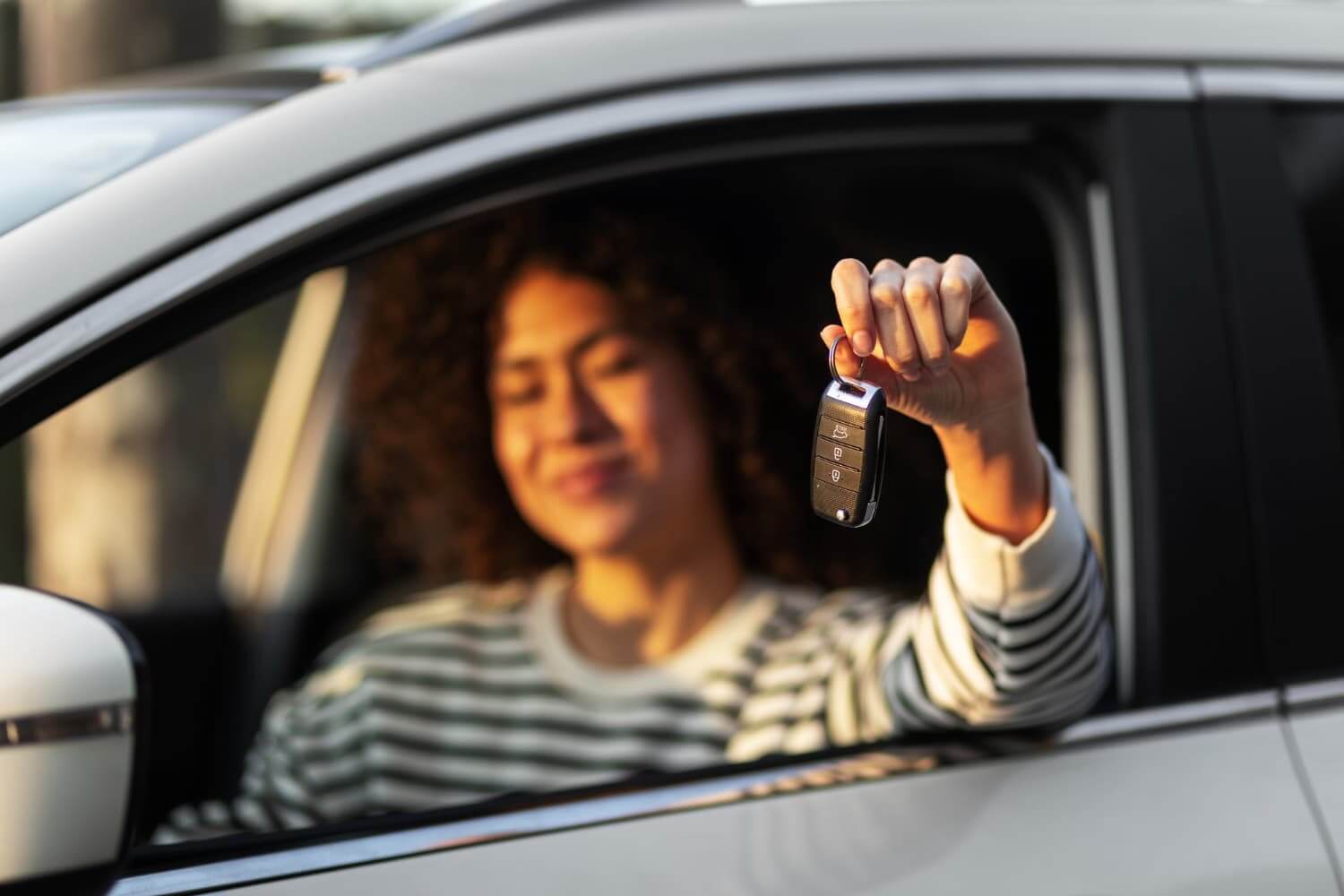 Mulher segurando uma chave de carro pela janela do veículo.