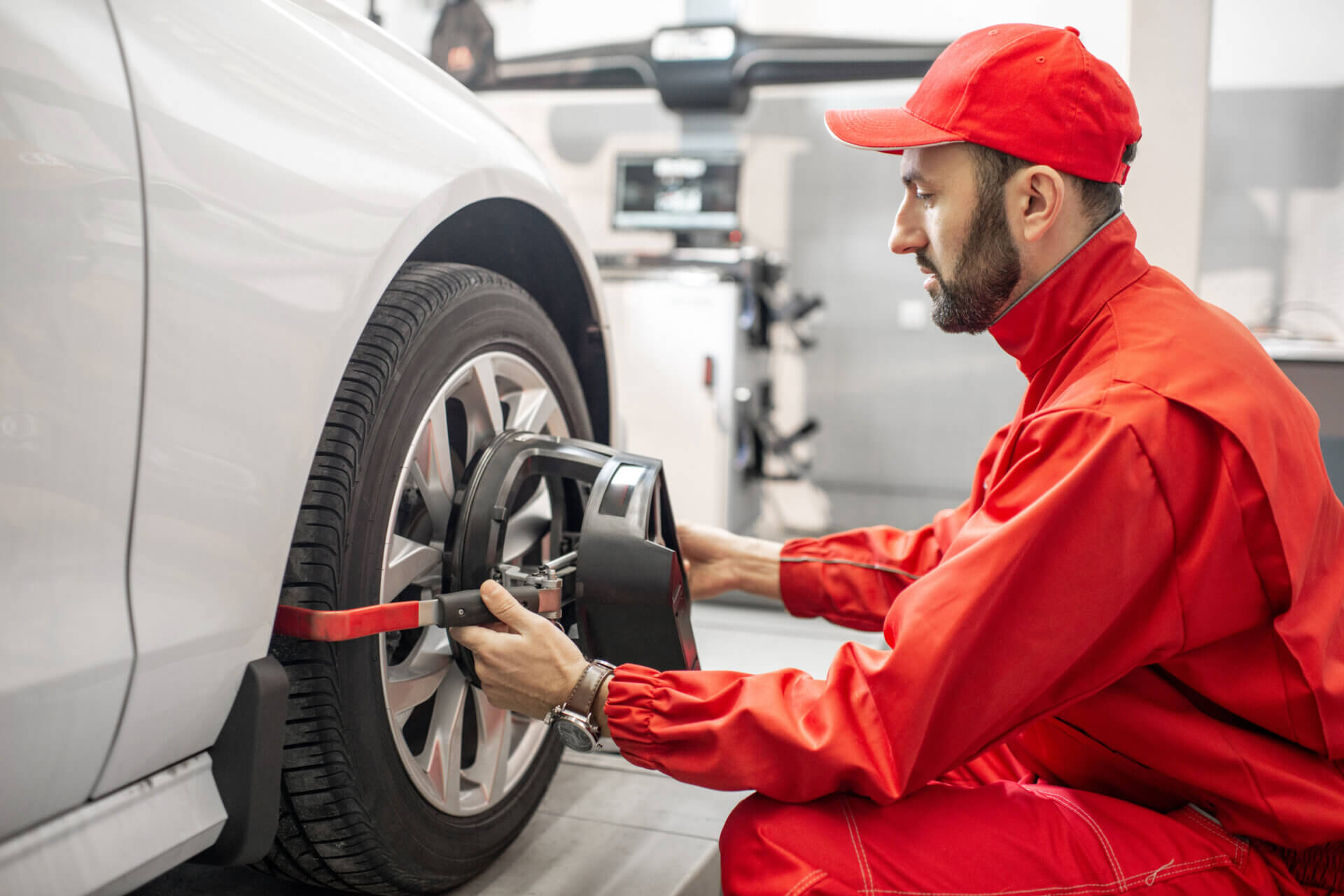 Pessoa de macacão e boné vermelho realizando o alinhamento e balanceamento de um carro branco.