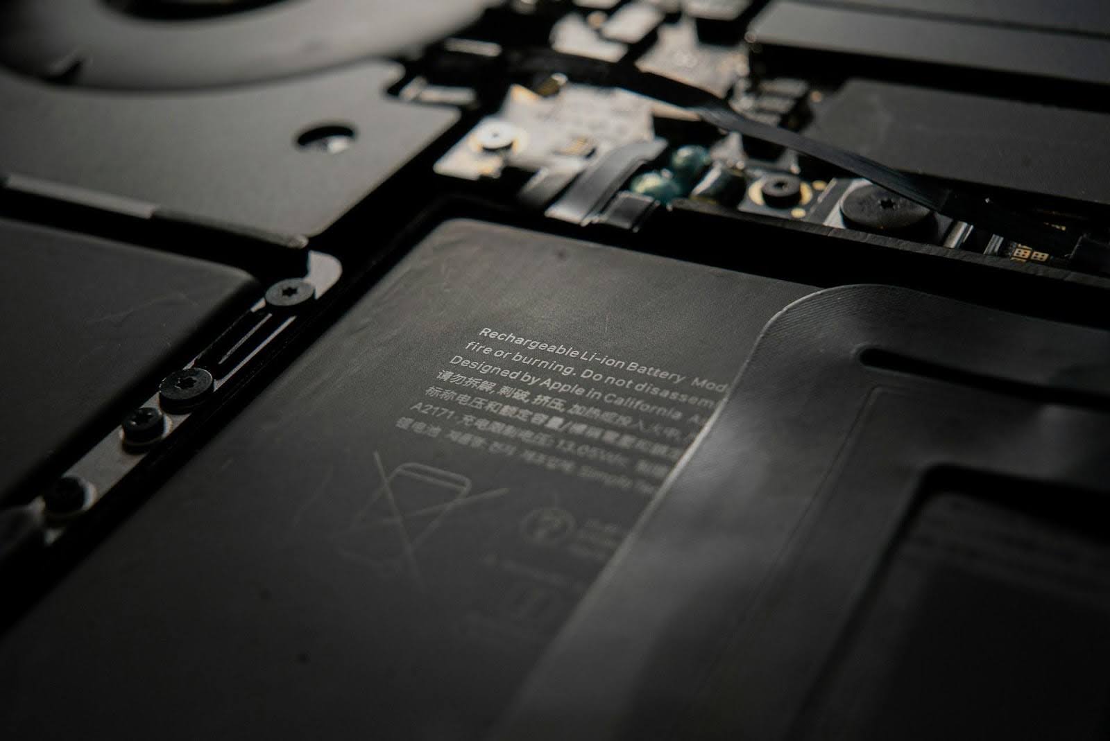 Close-up do interior de um notebook mostrando o pack de bateria de íon‑lítio e componentes eletrônicos ao redor, com inscrições técnicas visíveis na superfície.