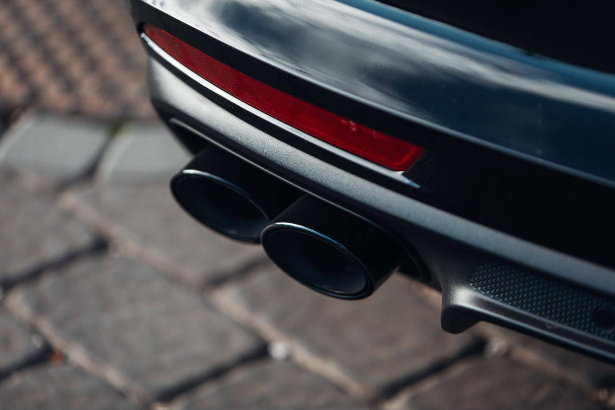Close em escapamento esportivo duplo de um carro preto.