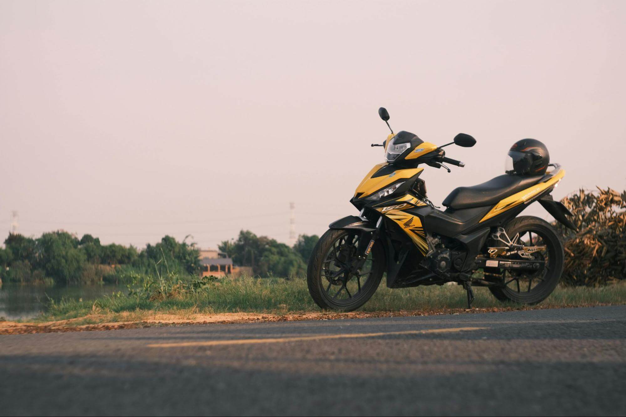 Moto amarela e preta com capacete no banco em meio à estrada