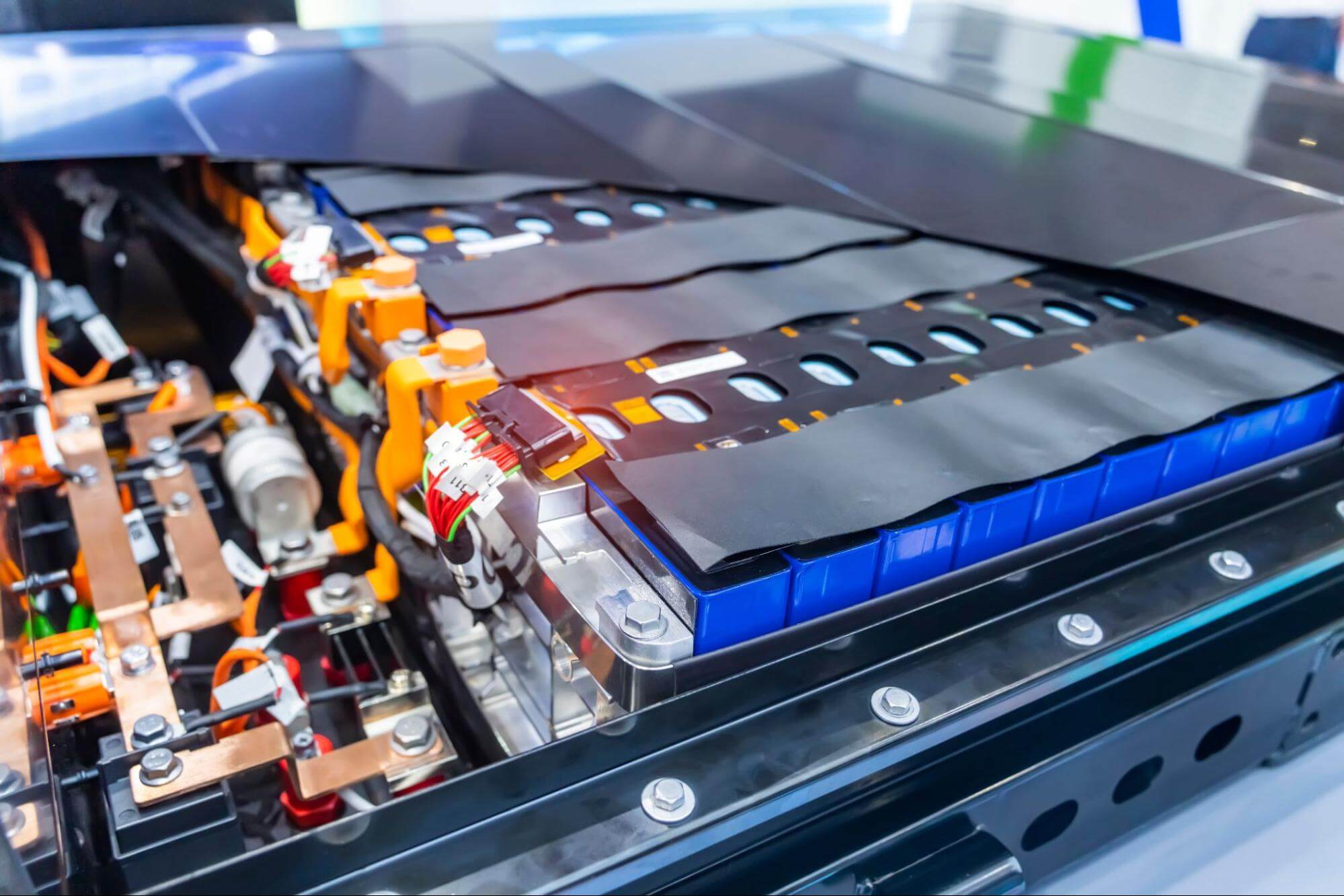 Foto detalhada mostrando o interior de uma bateria de veículo elétrico, com módulos de células individuais, barramentos de cobre e fiação de alta tensão visíveis.