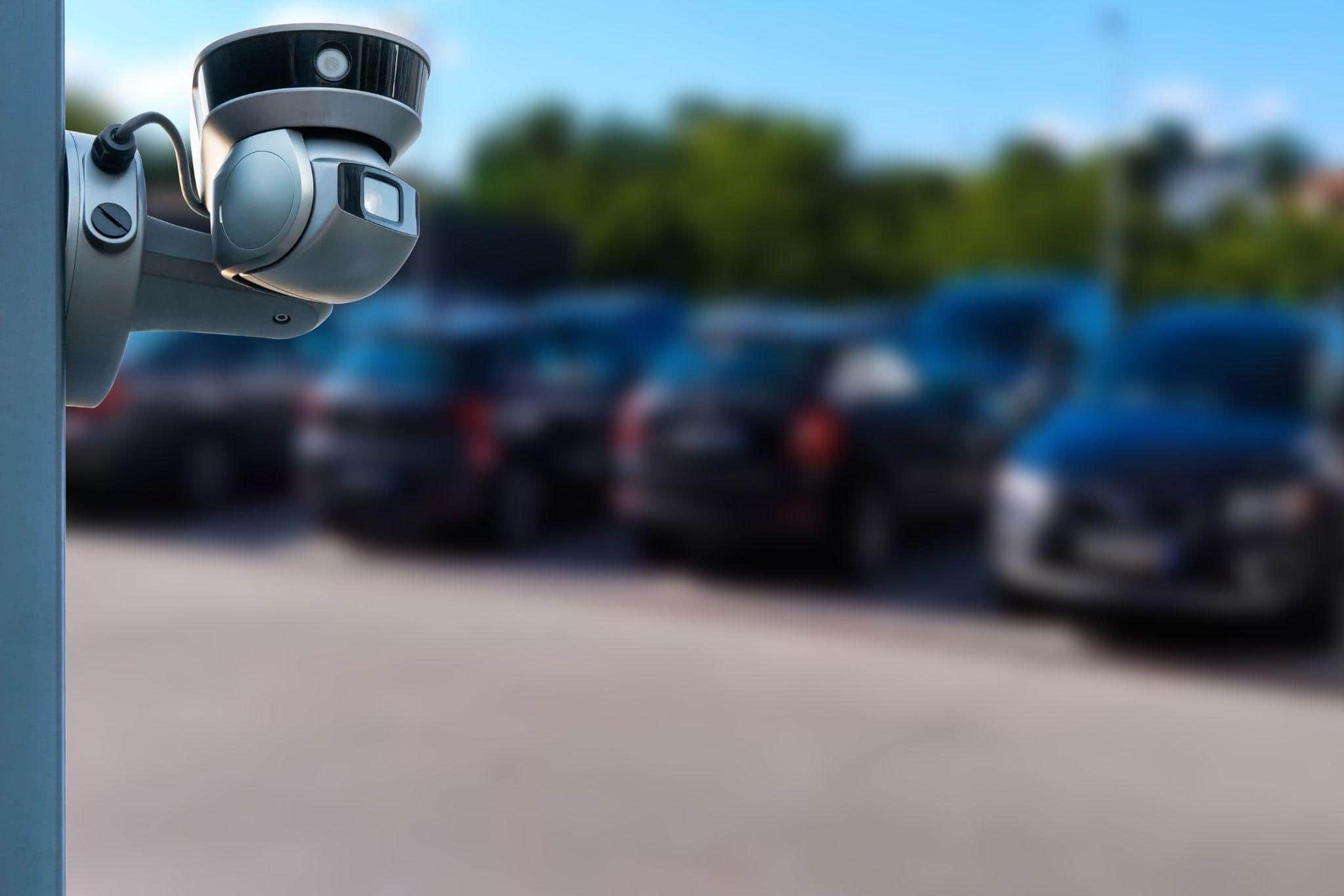 Câmera de segurança em foco com estacionamento desfocado ao fundo. 