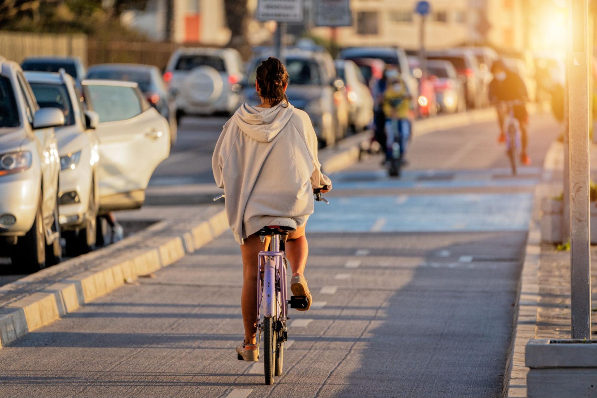 Mulher de moletom andando de bicicleta em ciclovia meio a cidade