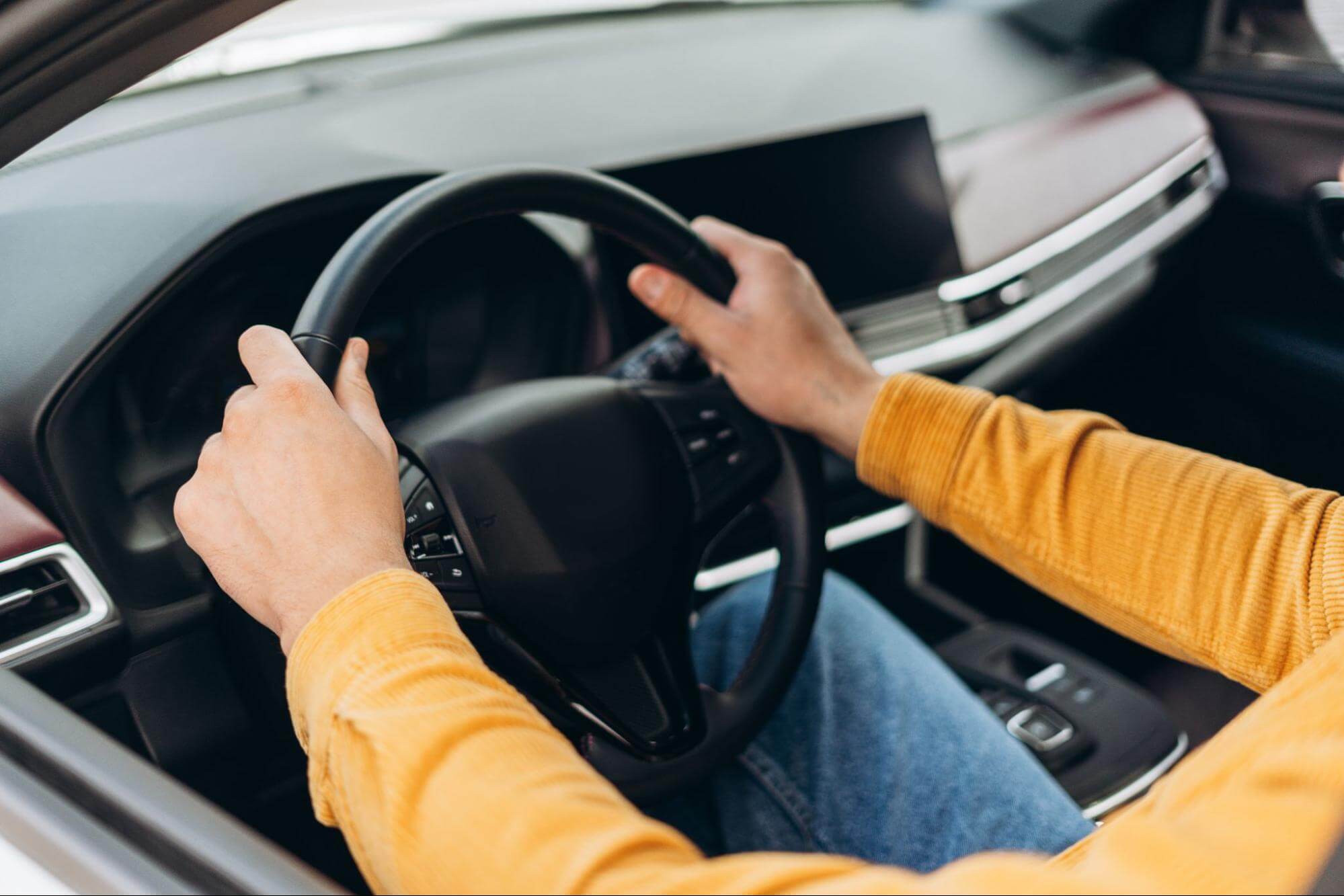 Pessoa com mangas longas amarelas segura um volante dentro de um carro