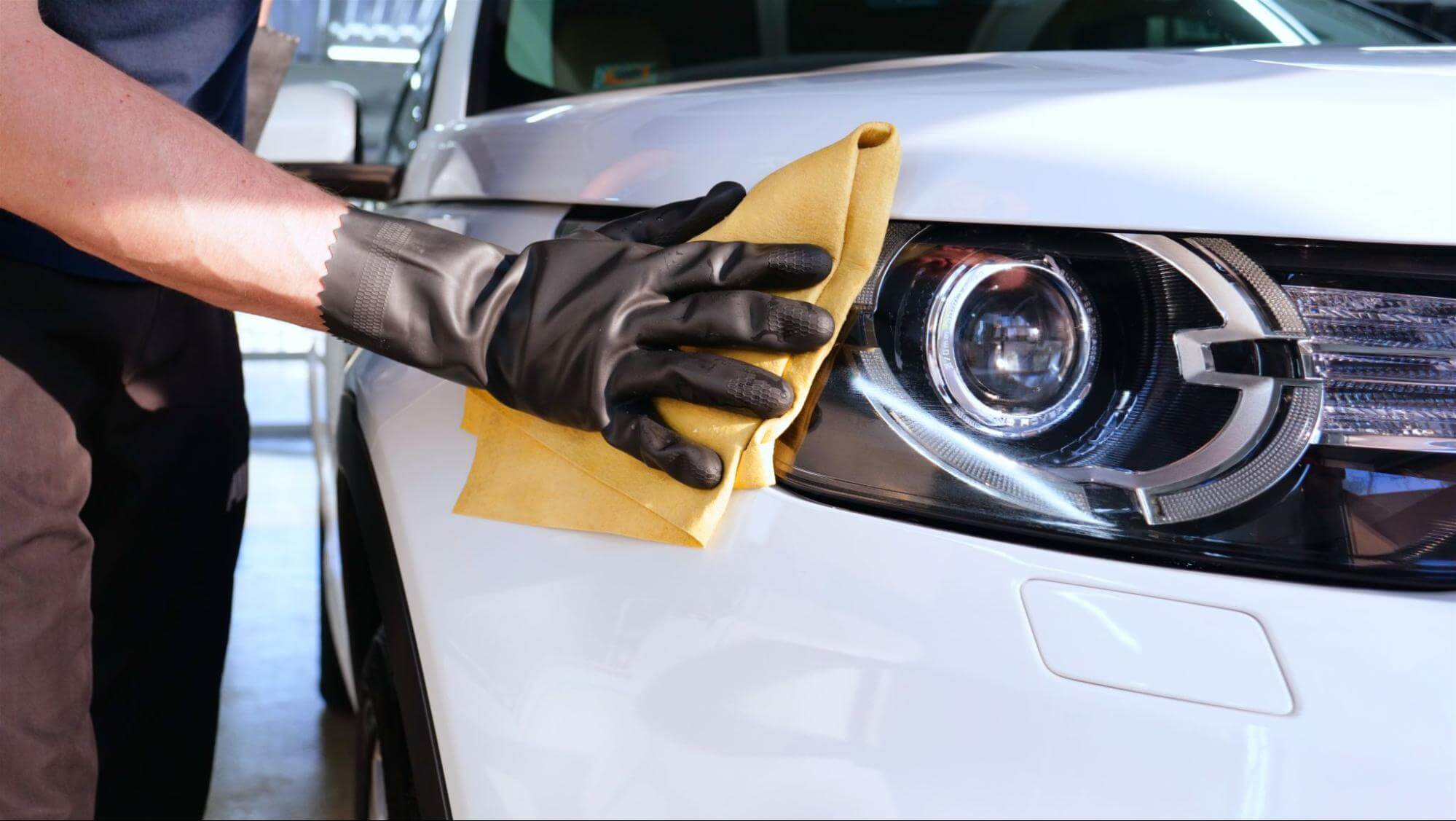 Pessoa limpa farol de carro branco com um pano amarelo. 