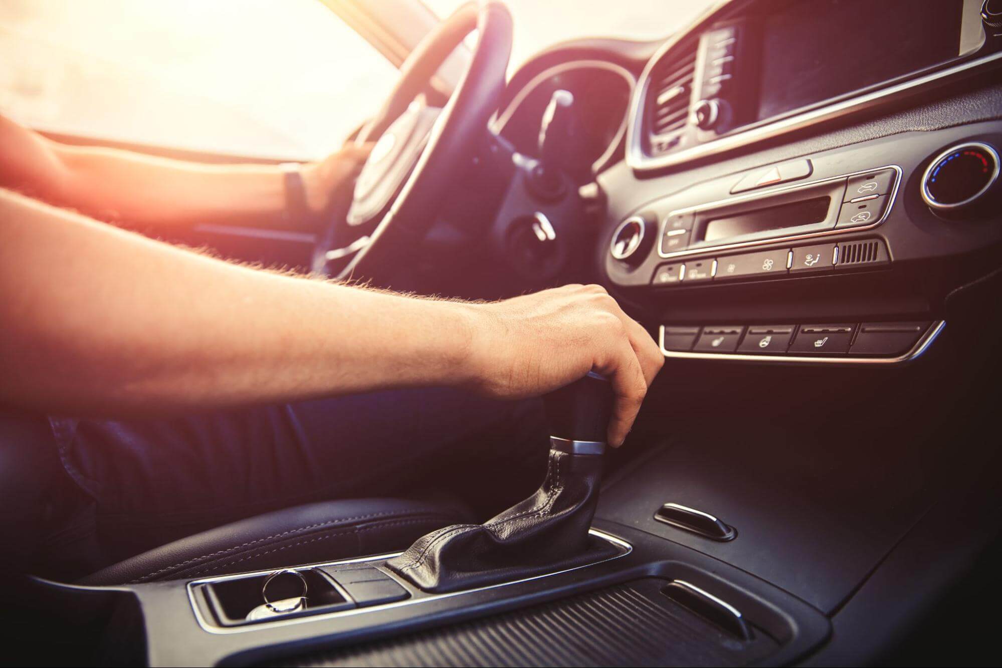 Pessoa com uma mão no câmbio e outra no volante de um carro. 