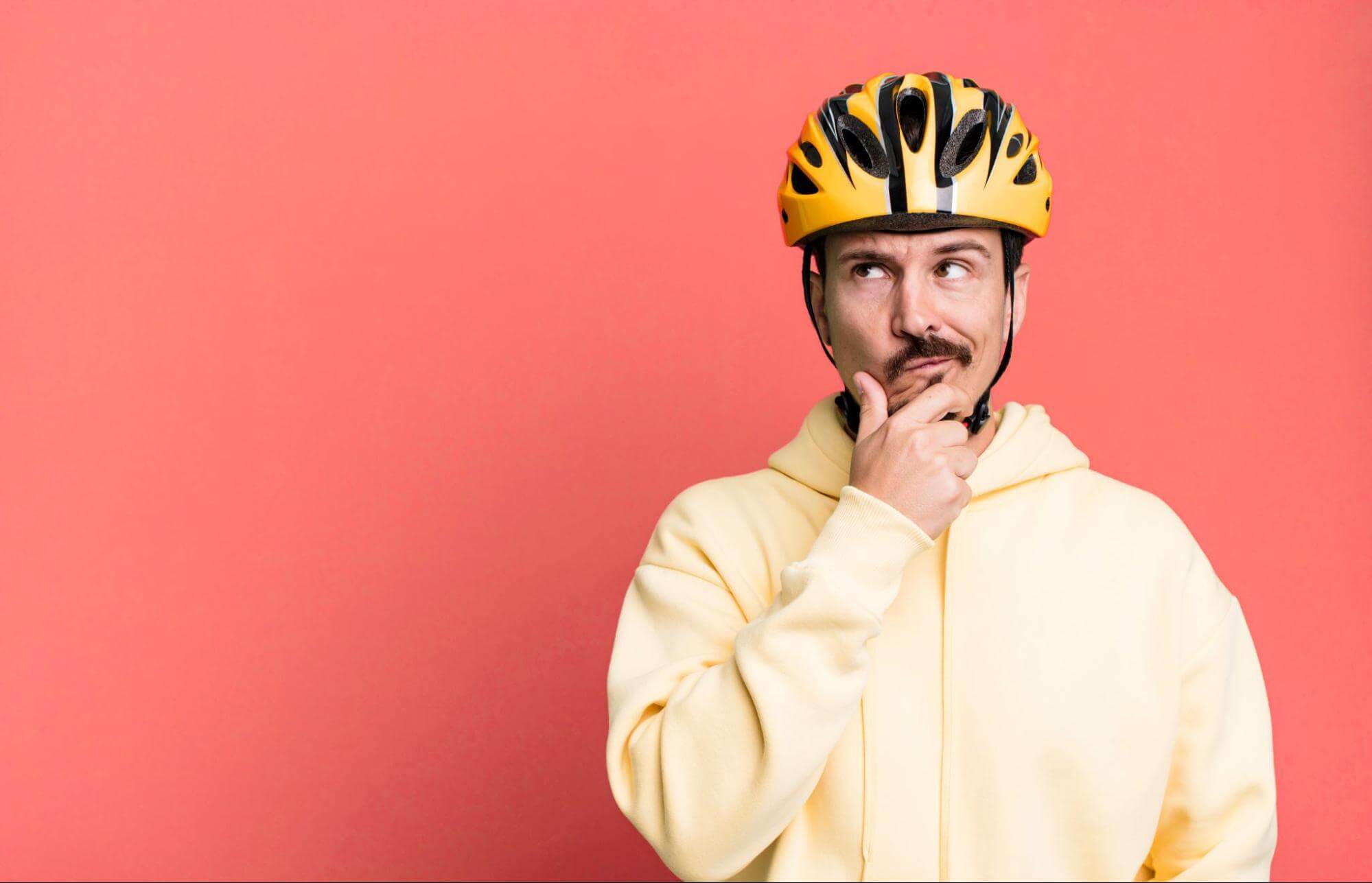 Homem posando com um capacete de bicicleta em amarelo e preto com polegar e indicador no queixo, em pose de quem está pensando.