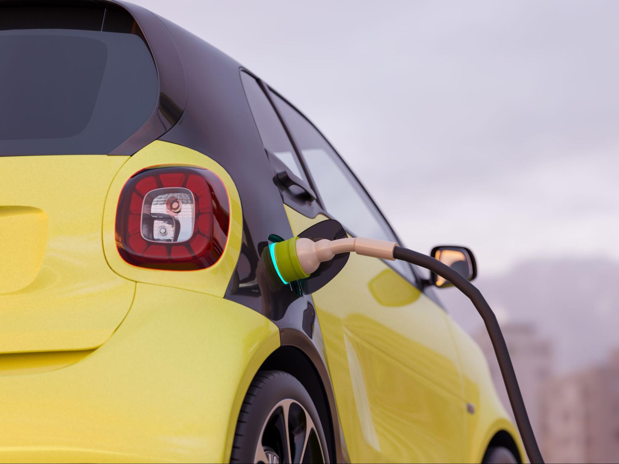 Carro elétrico em amarelo e preto sendo carregado por plug conector. 