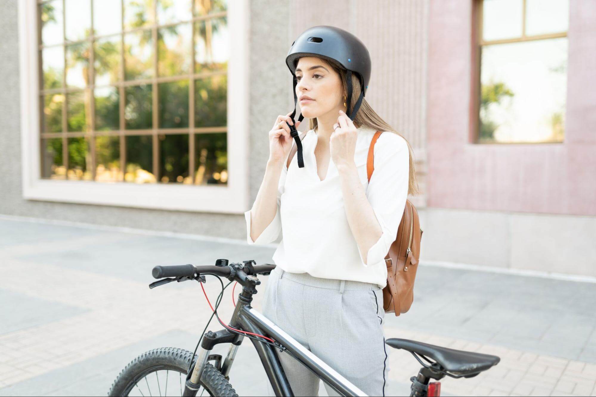 Mulher abotoando capacete de bicicleta em sua cabeça com uma bike preta à frente.