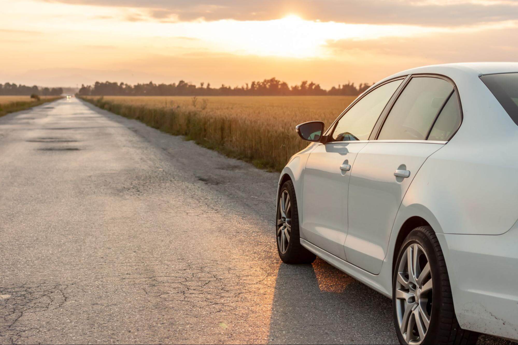 Carro branco em acostamento de uma estrada com pôr do sol ao fundo