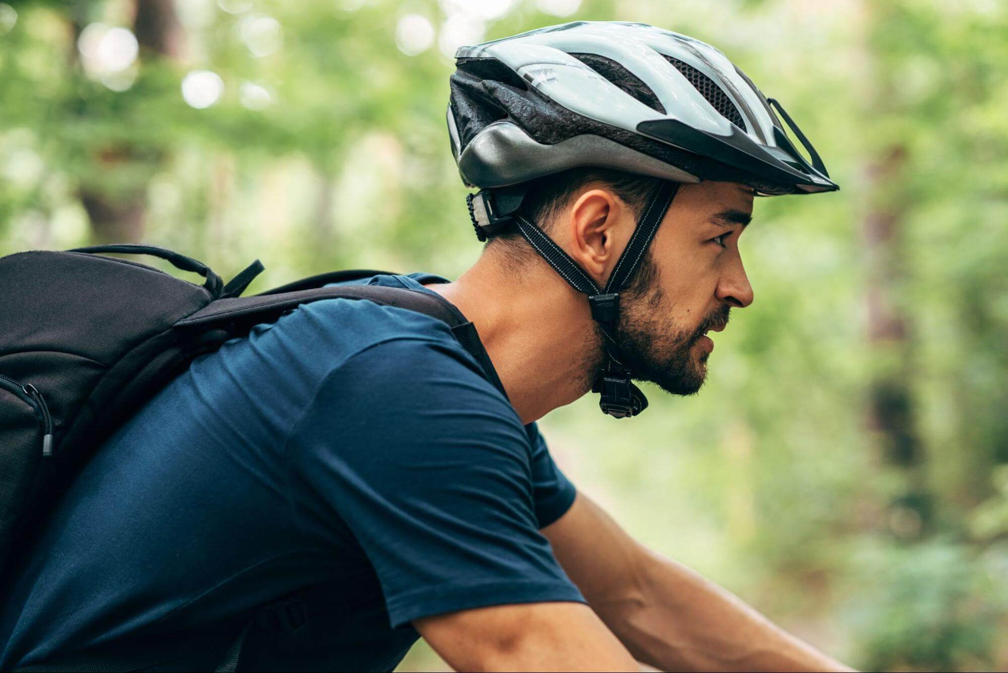 Homem de perfil com capacete de bicicleta enquanto pedala em fundo arborizado