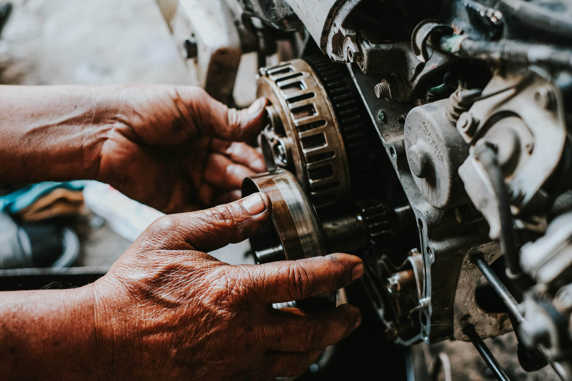 Mãos de um mecânico trabalhando nas engrenagens do motor de uma motocicleta.