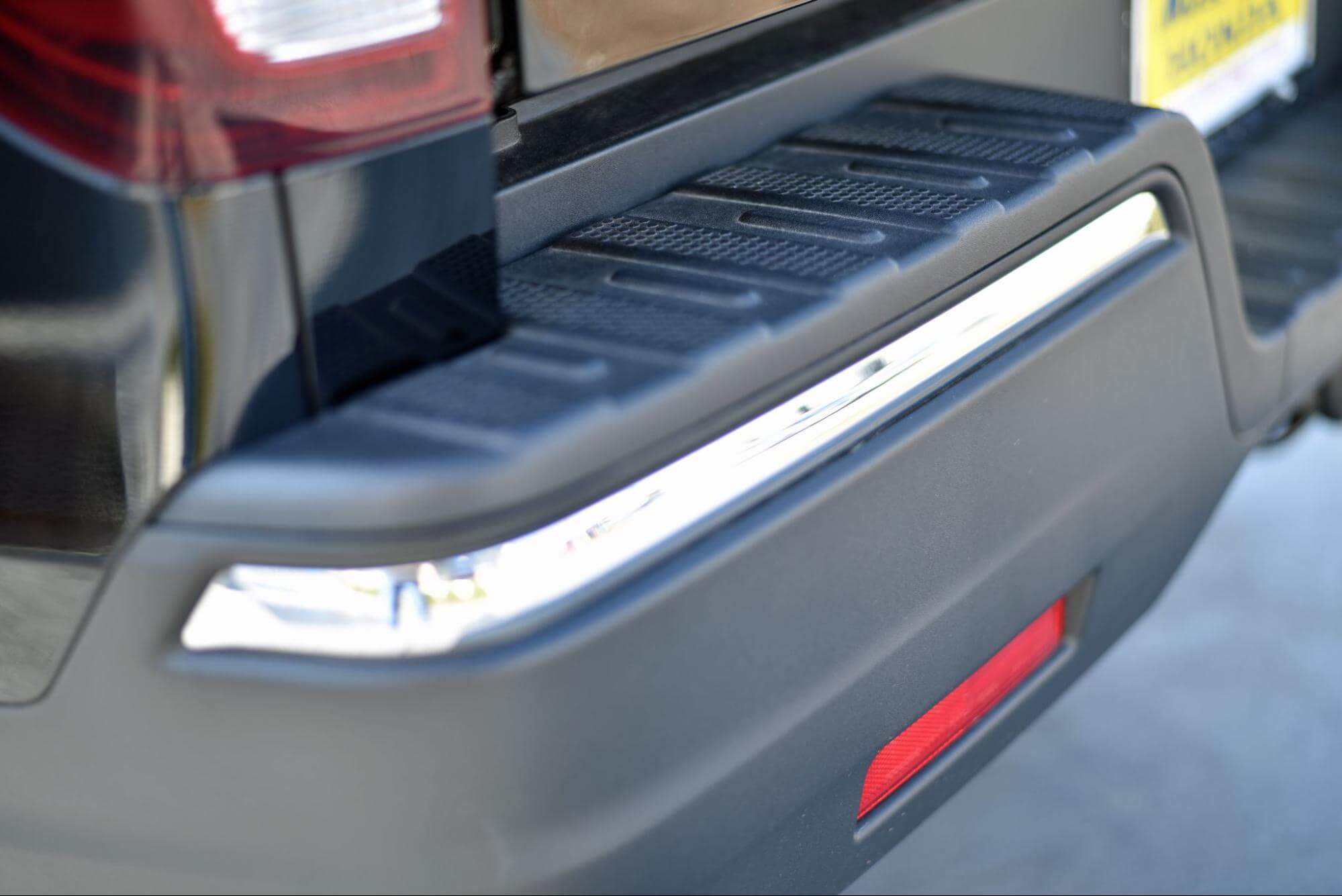 Para-choque traseiro preto de um veículo com friso cromado e detalhe em refletor vermelho.